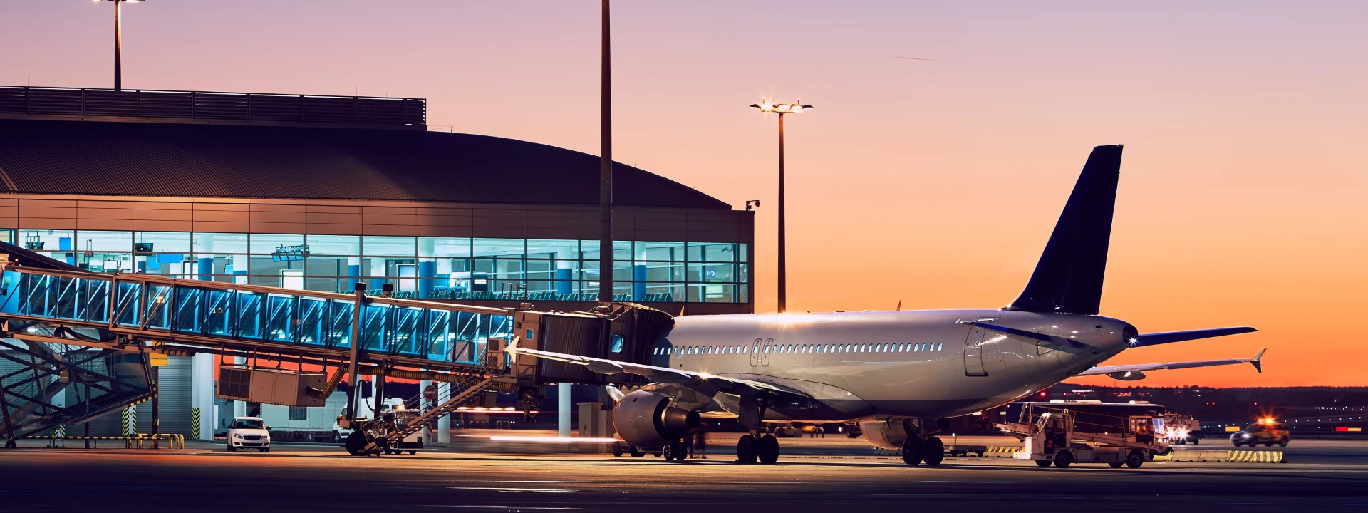 Commercial airplane parked at an airport terminal during sunset with a boarding bridge attached, representing aviation infrastructure, air travel, and logistics connectivity.